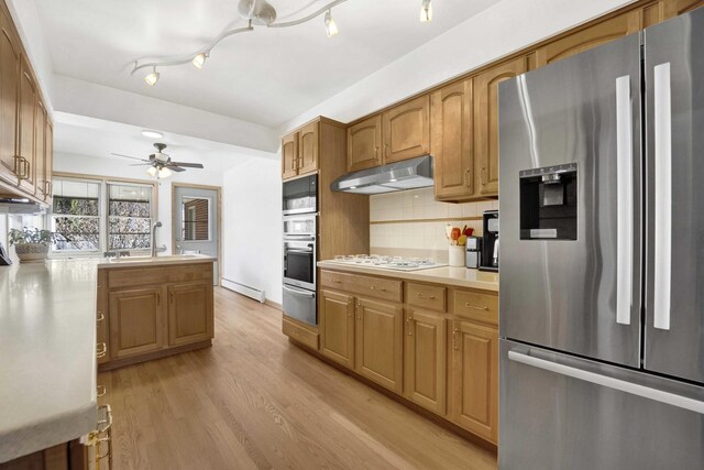 kitchen featuring appliances with stainless steel finishes, a sink, light countertops, under cabinet range hood, and a warming drawer
