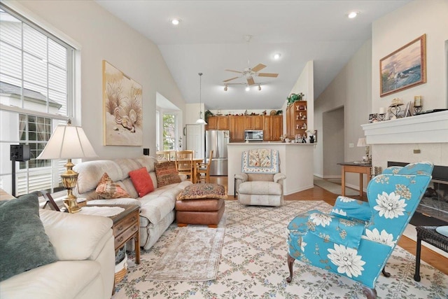 living room with a fireplace, a ceiling fan, light wood-type flooring, and lofted ceiling