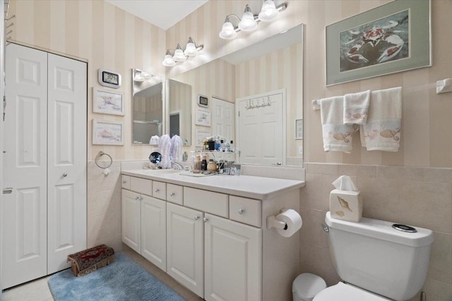 full bath featuring wainscoting, tile walls, toilet, and wallpapered walls