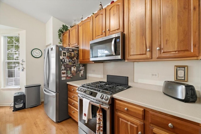 kitchen featuring light countertops, stainless steel appliances, brown cabinets, and light wood-style flooring