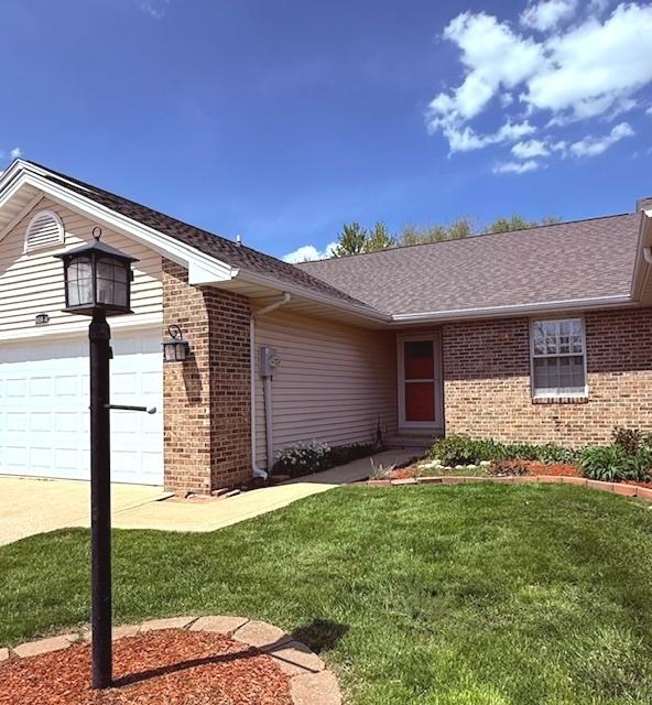 view of front of home with brick siding, a shingled roof, driveway, and a front yard
