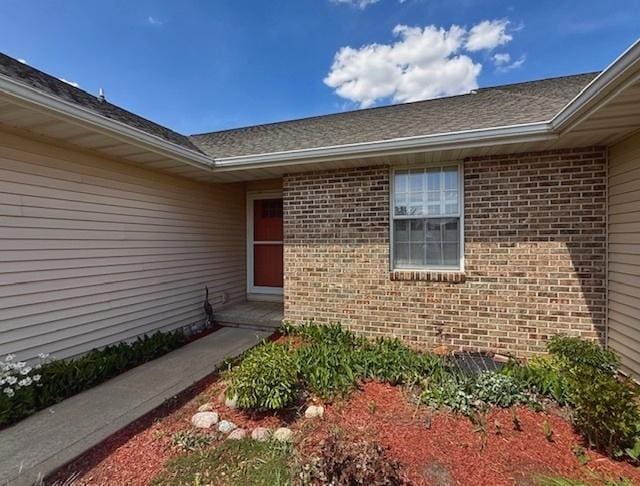 doorway to property featuring brick siding and roof with shingles