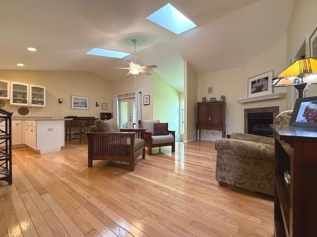living room with a ceiling fan, light wood-type flooring, lofted ceiling with skylight, and a fireplace
