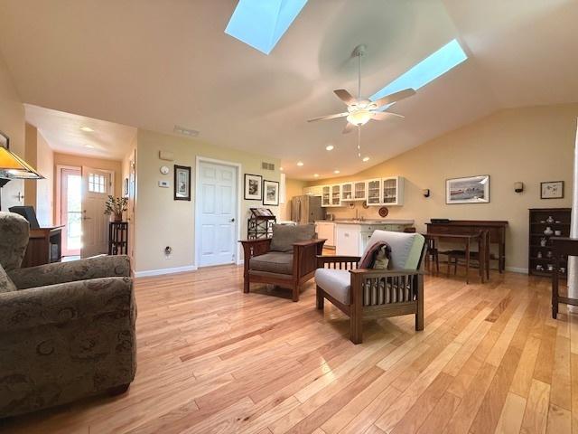living area with baseboards, a ceiling fan, light wood-style flooring, and vaulted ceiling with skylight