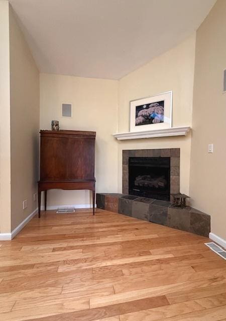 living room with baseboards, visible vents, wood finished floors, and a tile fireplace
