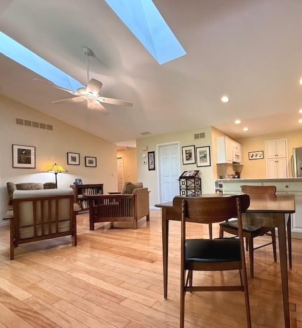dining area featuring visible vents, a ceiling fan, light wood finished floors, and lofted ceiling with skylight
