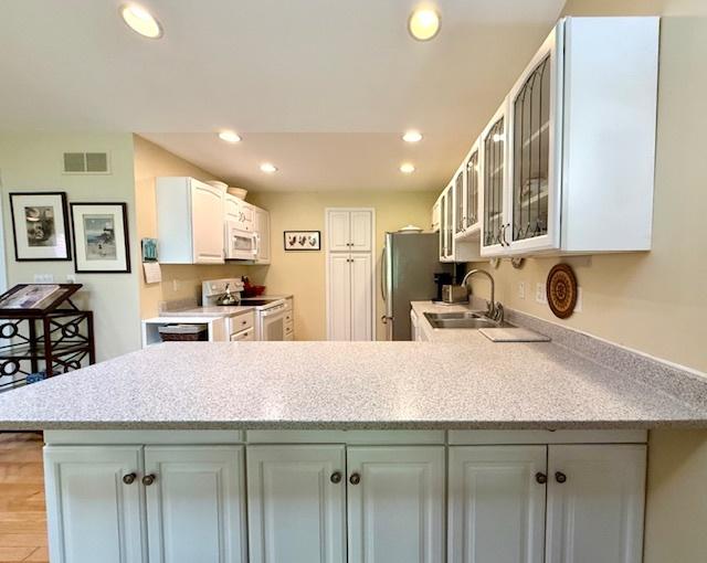 kitchen featuring a sink, white appliances, a peninsula, recessed lighting, and visible vents