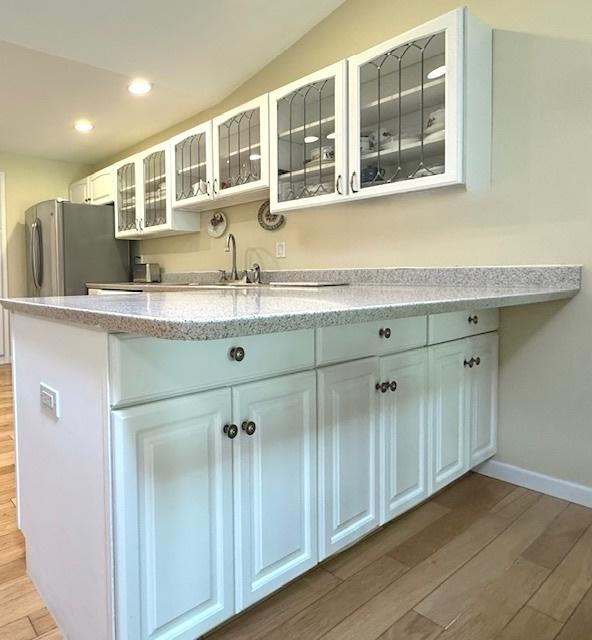 kitchen with freestanding refrigerator, glass insert cabinets, recessed lighting, white cabinetry, and light wood finished floors
