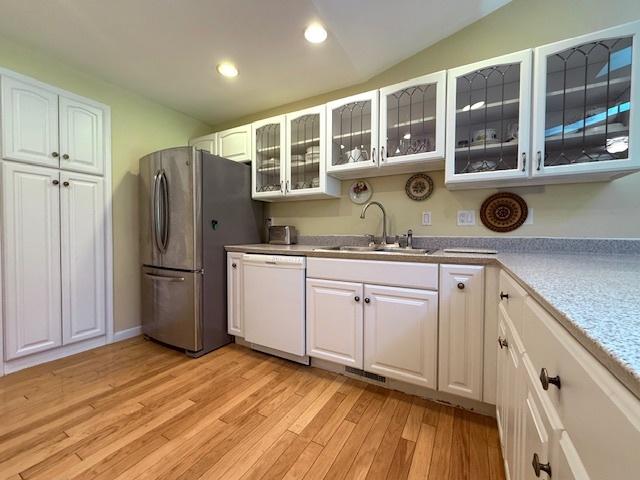 kitchen with white dishwasher, a sink, white cabinets, and freestanding refrigerator