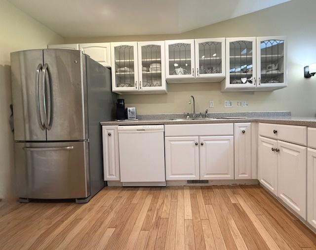 kitchen featuring white dishwasher, a sink, white cabinets, and freestanding refrigerator