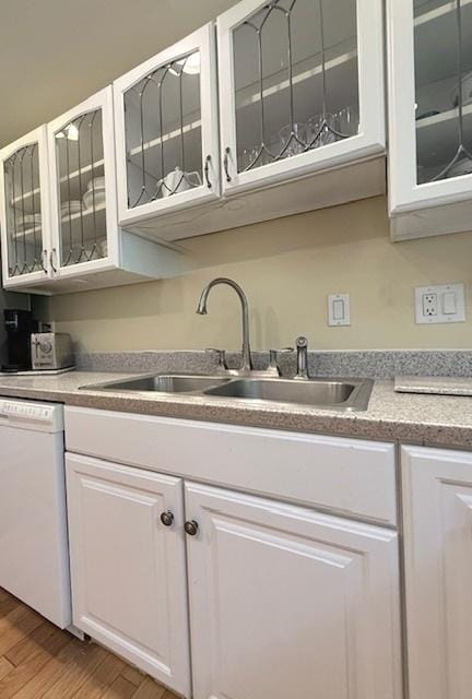 kitchen featuring white cabinets, a sink, light wood-style floors, dishwasher, and glass insert cabinets