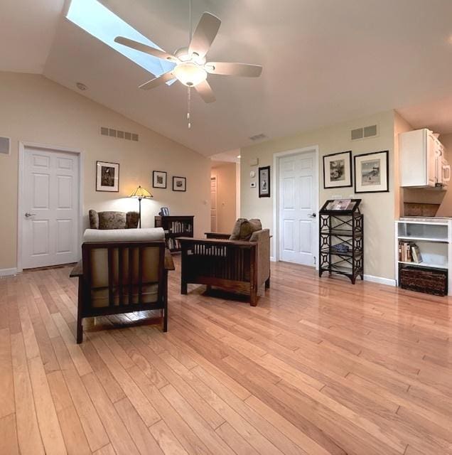 living room featuring a ceiling fan, lofted ceiling with skylight, light wood-style flooring, and visible vents
