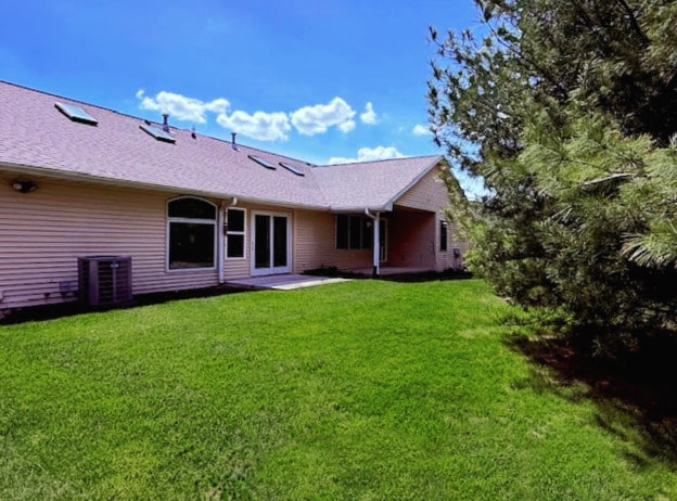 rear view of house featuring a lawn and central AC