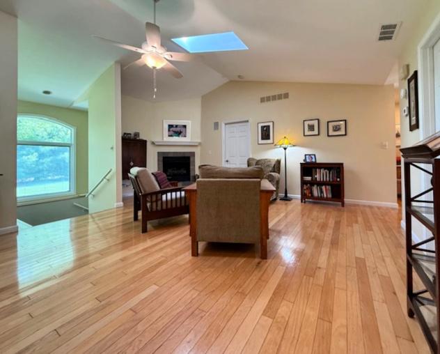 living room featuring a tiled fireplace, a ceiling fan, light wood-style flooring, and visible vents