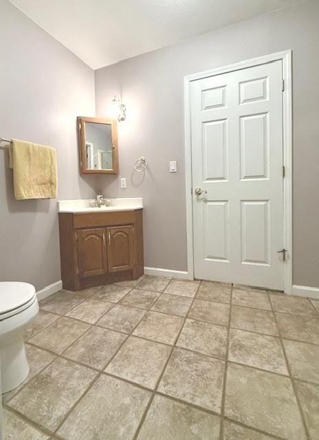 half bath with tile patterned flooring, vanity, toilet, baseboards, and vaulted ceiling