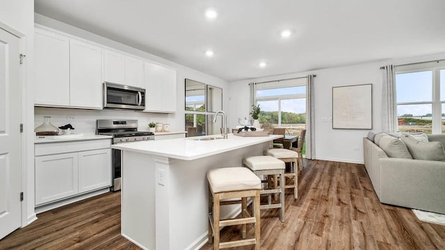 kitchen with a breakfast bar, a center island with sink, dark wood-type flooring, a sink, and appliances with stainless steel finishes