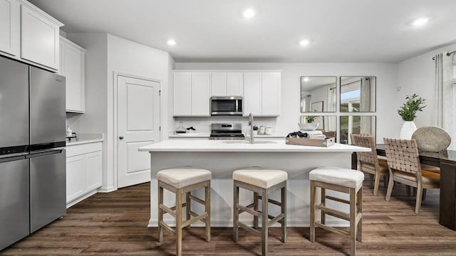 kitchen featuring a kitchen bar, appliances with stainless steel finishes, a sink, light countertops, and dark wood-style floors