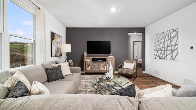 living area with visible vents, an accent wall, baseboards, and wood finished floors