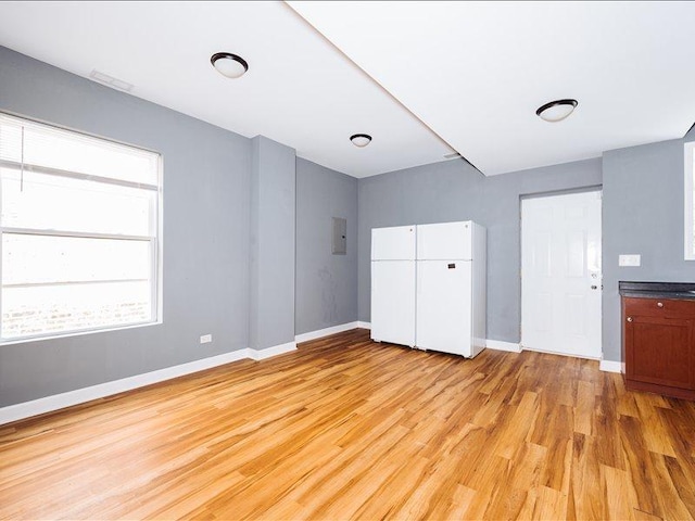 unfurnished bedroom featuring a closet, baseboards, electric panel, and light wood-style floors