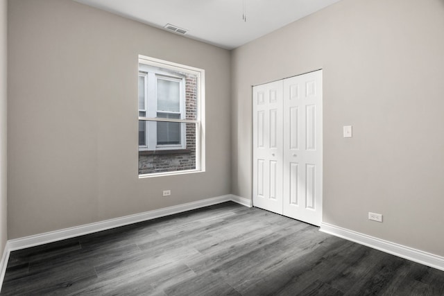 unfurnished bedroom featuring baseboards, a closet, dark wood-style flooring, and visible vents