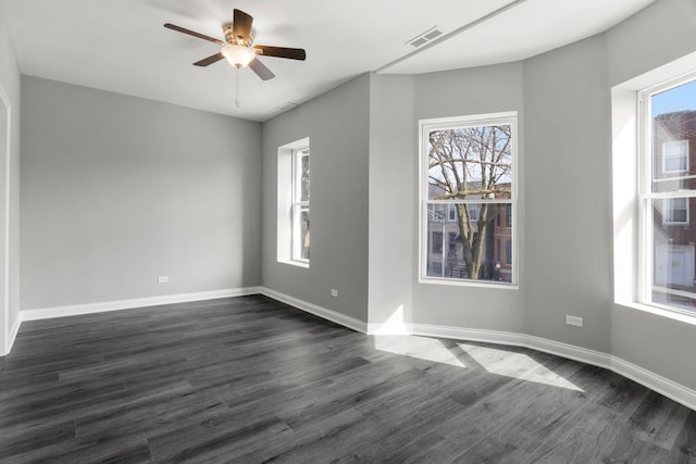 empty room with dark wood-type flooring, a ceiling fan, baseboards, and visible vents
