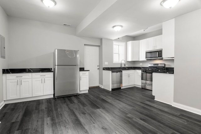 kitchen featuring appliances with stainless steel finishes, dark countertops, a sink, baseboards, and dark wood-style floors
