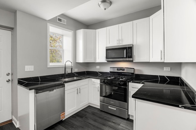 kitchen featuring dark wood-style flooring, dark countertops, white cabinets, a sink, and appliances with stainless steel finishes