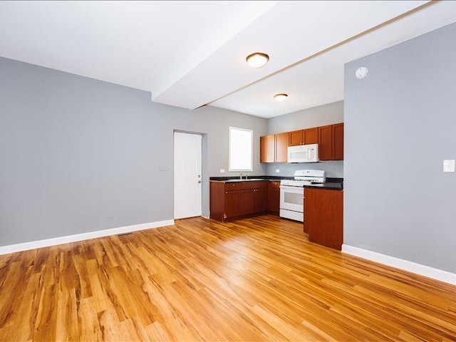 kitchen with white appliances, dark countertops, a sink, and light wood-style floors