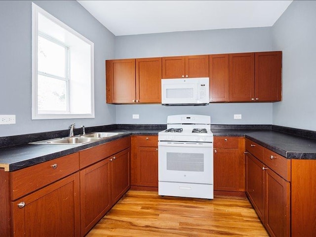 kitchen featuring brown cabinets, dark countertops, a sink, white appliances, and light wood-type flooring