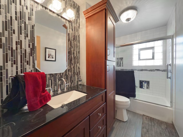 full bathroom featuring toilet, tile walls, wood finished floors, vanity, and shower / bath combination with glass door