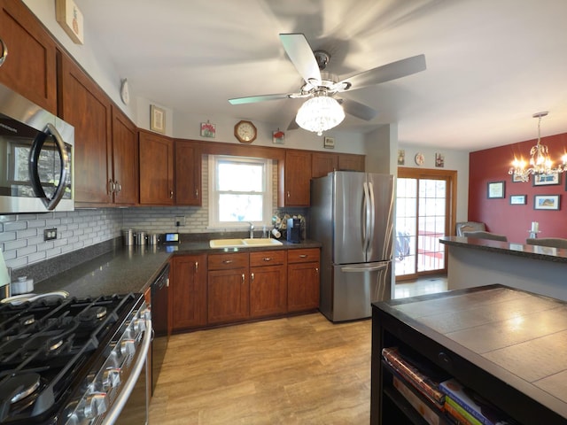 kitchen with a sink, ceiling fan with notable chandelier, appliances with stainless steel finishes, backsplash, and light wood-style floors