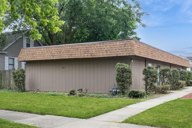 view of side of home with a shingled roof, a lawn, and mansard roof