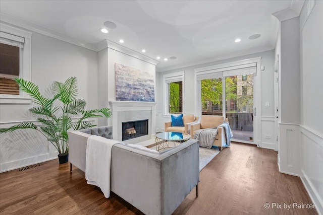 living area featuring crown molding, a decorative wall, a fireplace, recessed lighting, and wood finished floors