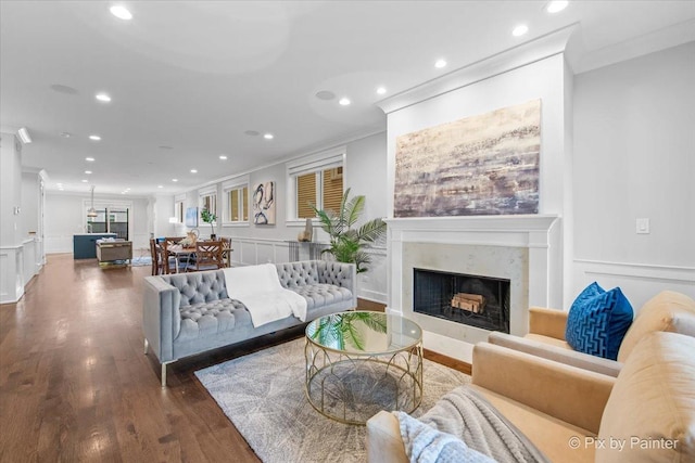 living room featuring a fireplace, wood finished floors, ornamental molding, a decorative wall, and recessed lighting