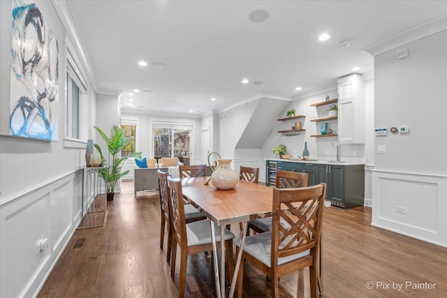 dining space with crown molding, a decorative wall, recessed lighting, dark wood-type flooring, and a wainscoted wall