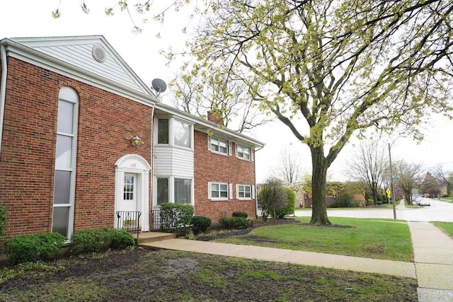 view of front facade with brick siding, a chimney, and a front yard