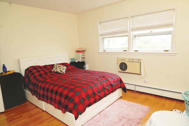 bedroom featuring a wall mounted AC, wood finished floors, and a baseboard radiator