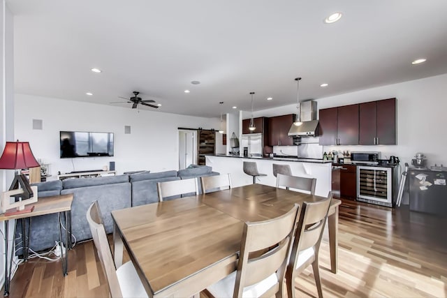 dining room with beverage cooler, light wood-style floors, ceiling fan, recessed lighting, and a barn door