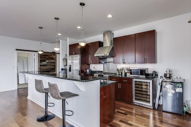 kitchen with a breakfast bar area, dark wood finished floors, wall chimney exhaust hood, stainless steel appliances, and wine cooler