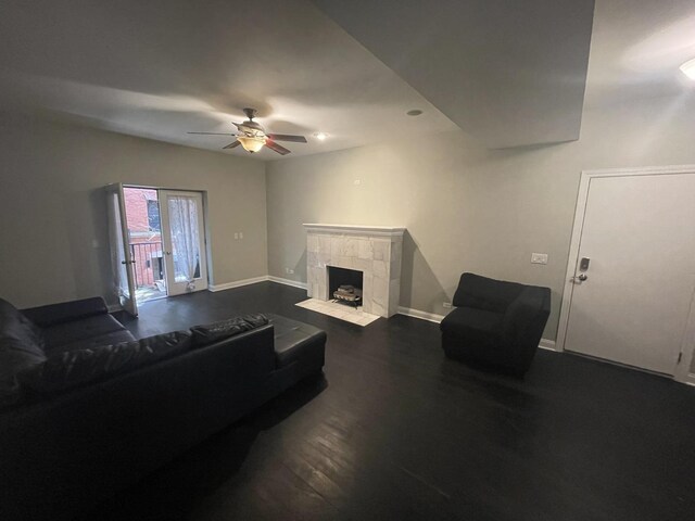 living area featuring baseboards, dark wood finished floors, ceiling fan, and a fireplace