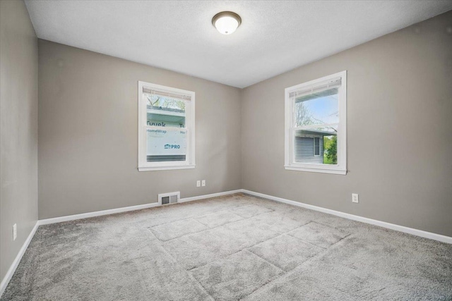 carpeted spare room with baseboards, visible vents, and plenty of natural light