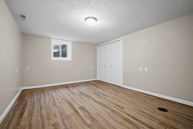unfurnished bedroom with a textured ceiling, baseboards, wood finished floors, visible vents, and a closet