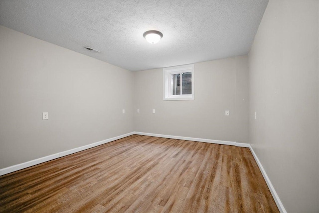 spare room featuring baseboards, a textured ceiling, wood finished floors, and visible vents