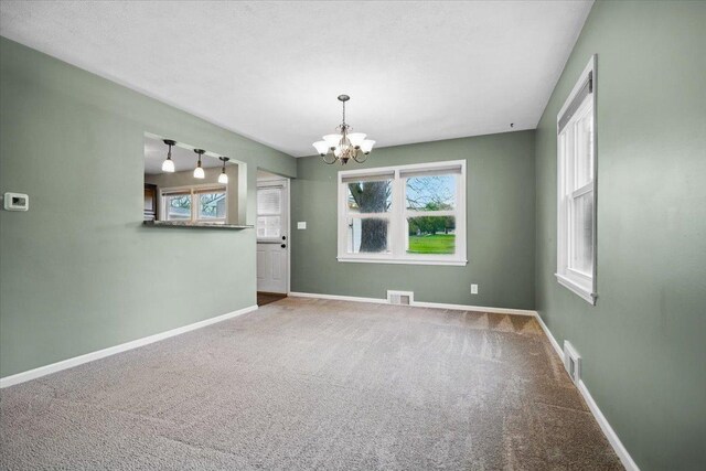 unfurnished room with visible vents, a chandelier, a wealth of natural light, and carpet