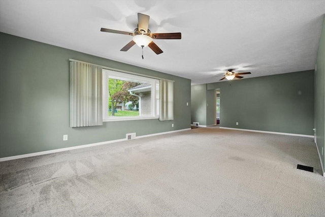 carpeted spare room with visible vents, baseboards, and ceiling fan