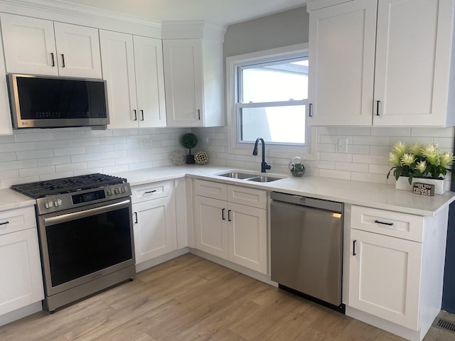 kitchen with appliances with stainless steel finishes, a sink, light countertops, white cabinets, and light wood finished floors