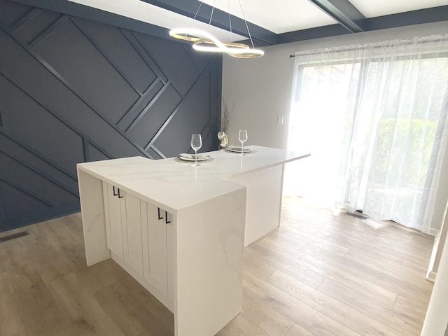 kitchen with a kitchen island, beam ceiling, light wood finished floors, an inviting chandelier, and white cabinetry