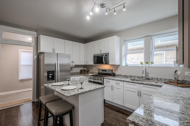 kitchen with dark wood-style flooring, light stone countertops, a sink, a center island, and stainless steel appliances