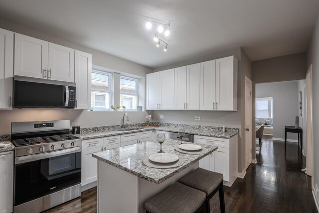 kitchen with white cabinets, a sink, a kitchen breakfast bar, stainless steel appliances, and dark wood-type flooring
