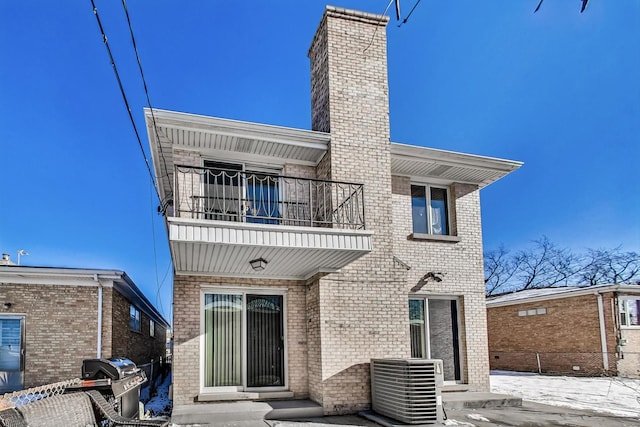 back of property with a chimney, brick siding, central AC, a balcony, and entry steps